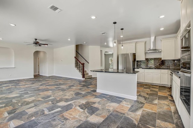 309 Camperdown Elm Dr, Austin, TX 78748 - kitchen with appliances with stainless steel finishes, wall chimney exhaust hood, arched walkways, dark countertops, and stone tile flooring