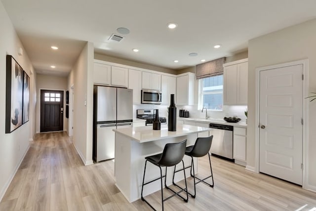 2420 Ekvall Dr, Round Rock, TX 78665 - kitchen featuring appliances with stainless steel finishes, a kitchen breakfast bar, light wood-style flooring, white cabinetry, and recessed lighting