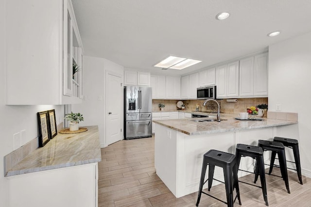 13517 Carlos Fifth Ct, Corpus Christi, TX 78418 - kitchen with appliances with stainless steel finishes, a peninsula, light wood-style floors, backsplash, and white cabinets