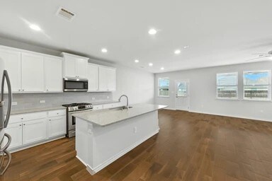 17320 Calipatria Ln, Pflugerville, TX 78660 - kitchen with appliances with stainless steel finishes, open floor plan, dark wood-style floors, a center island with sink, and recessed lighting