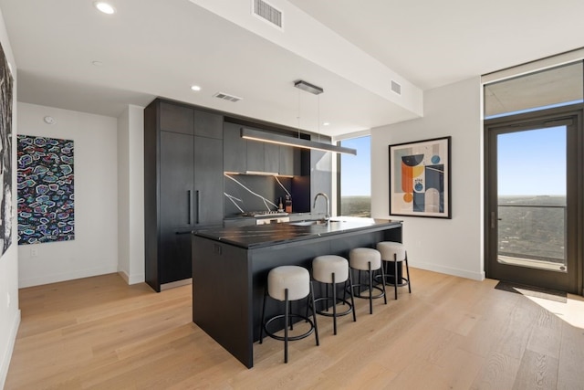 44 E Ave Unit 3801, Austin, TX 78701 - kitchen with modern cabinets, a kitchen bar, dark countertops, an island with sink, and light wood-type flooring
