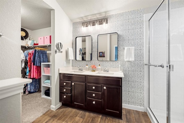 118 Craft St, Hutto, TX 78634 - bathroom with wood finished floors, double vanity, a stall shower, a textured ceiling, and a walk in closet