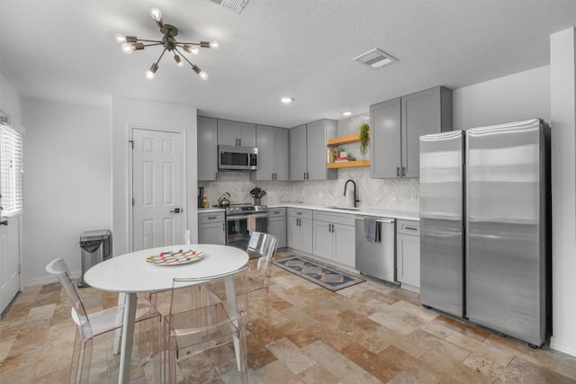 1509 Strickland Dr, Austin, TX 78748 - kitchen with stainless steel appliances, gray cabinets, open shelves, tasteful backsplash, and stone finish floors