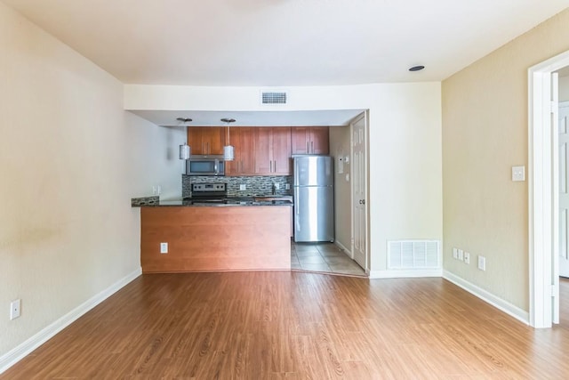 7685 Northcross Dr Unit 901, Austin, TX 78757 - kitchen with appliances with stainless steel finishes, a peninsula, decorative backsplash, wood finished floors, and brown cabinets