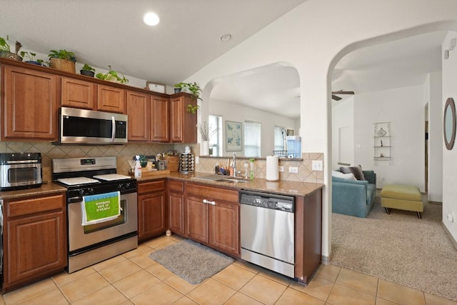 11012 Short Springs Dr, Austin, TX 78754 - kitchen featuring appliances with stainless steel finishes, brown cabinetry, tasteful backsplash, arched walkways, and vaulted ceiling