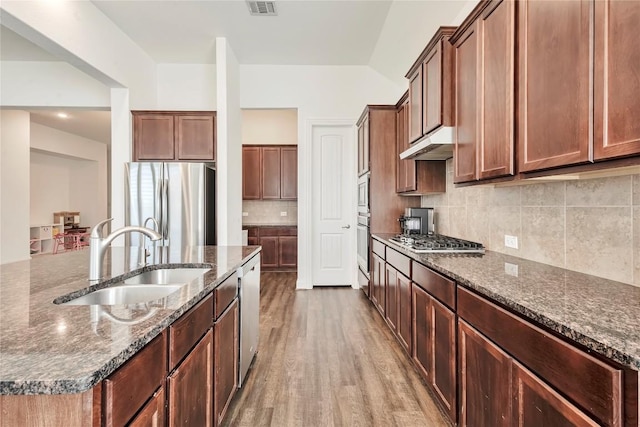 817 Clear Spring Ln, Leander, TX 78641 - kitchen with appliances with stainless steel finishes, under cabinet range hood, a kitchen island with sink, wood finished floors, and backsplash