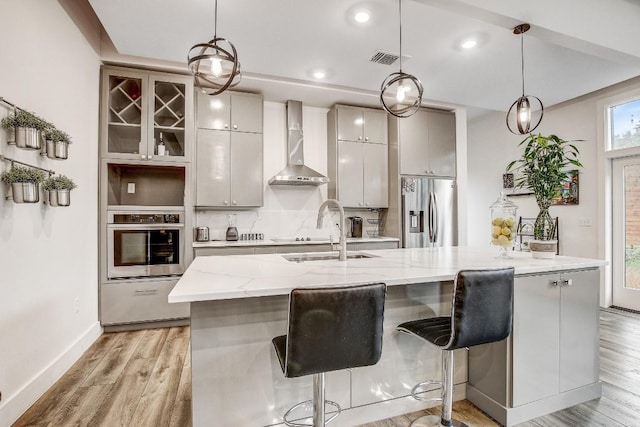 11300 Lake Dr, Austin, TX 78748 - kitchen with appliances with stainless steel finishes, wall chimney range hood, a center island with sink, light wood-style flooring, and a kitchen breakfast bar