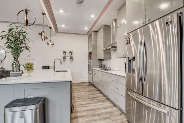 11300 Lake Dr, Austin, TX 78748 - kitchen featuring stainless steel appliances, wall chimney exhaust hood, gray cabinetry, light wood-type flooring, and light stone counters