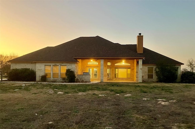 129 S Abrego Xing S, Floresville, TX 78114 - back of property at dusk featuring stone siding, a chimney, and a porch