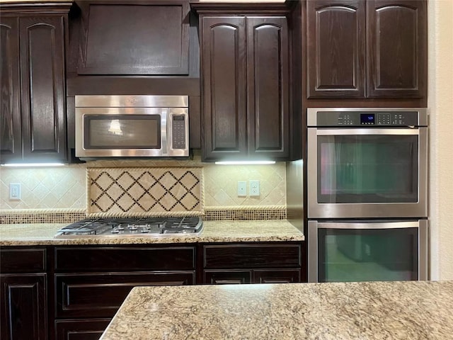129 S Abrego Xing S, Floresville, TX 78114 - kitchen with stainless steel appliances, dark brown cabinetry, tasteful backsplash, and light stone counters
