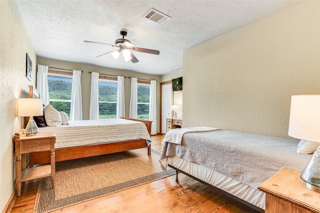 2308 Flite Acres Rd, Wimberley, TX 78676 - bedroom featuring a textured wall, a textured ceiling, wood finished floors, and ceiling fan