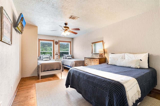 2308 Flite Acres Rd, Wimberley, TX 78676 - bedroom with a textured wall, light wood finished floors, a ceiling fan, and a textured ceiling