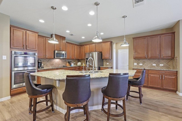 1124 Calla Lily Blvd, Leander, TX 78641 - kitchen featuring appliances with stainless steel finishes, a large island with sink, brown cabinets, tasteful backsplash, and light wood-style floors