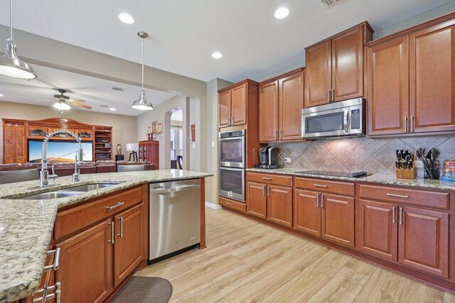 1124 Calla Lily Blvd, Leander, TX 78641 - kitchen with stainless steel appliances, arched walkways, light wood-type flooring, brown cabinets, and recessed lighting