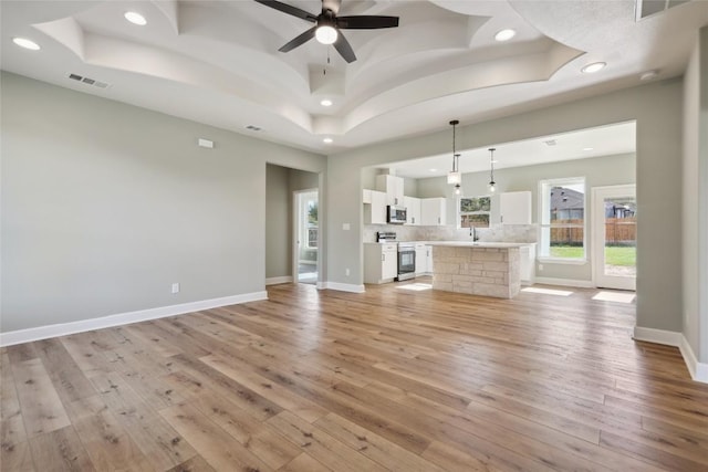109 Creek Side Dr, Bastrop, TX 78602 - unfurnished living room featuring a tray ceiling, recessed lighting, light wood-style floors, and ceiling fan