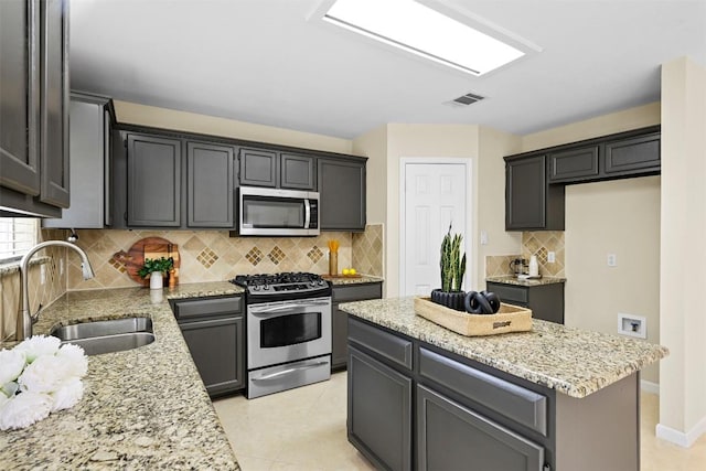 3528 Ruby Red Dr, Austin, TX 78728 - kitchen featuring appliances with stainless steel finishes, light stone countertops, a center island, tasteful backsplash, and light tile patterned floors