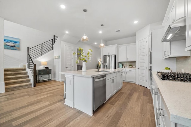 913 Landing Ln, Leander, TX 78641 - kitchen with under cabinet range hood, appliances with stainless steel finishes, light wood finished floors, backsplash, and white cabinets