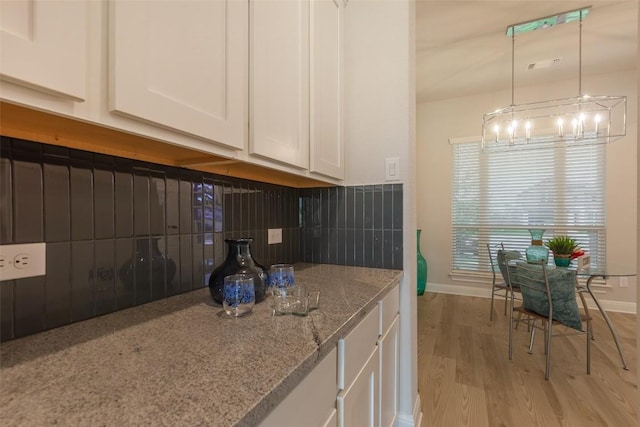 103 Periwinkle Ln, Bastrop, TX 78602 - kitchen featuring white cabinetry, a chandelier, light wood-style flooring, decorative backsplash, and light stone countertops