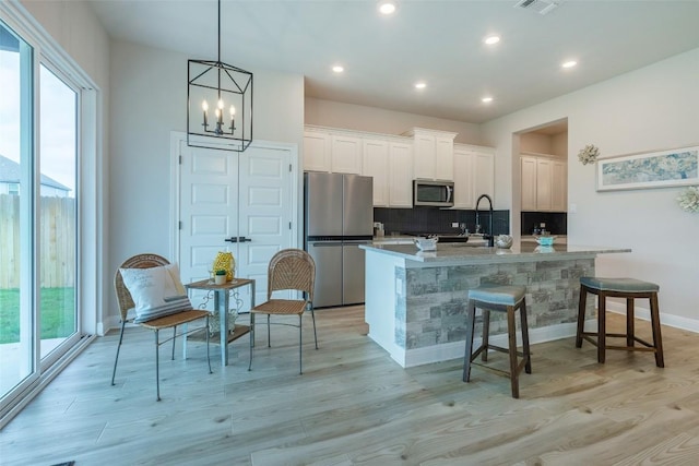 103 Periwinkle Ln, Bastrop, TX 78602 - kitchen with appliances with stainless steel finishes, decorative backsplash, an island with sink, white cabinets, and light wood-style flooring
