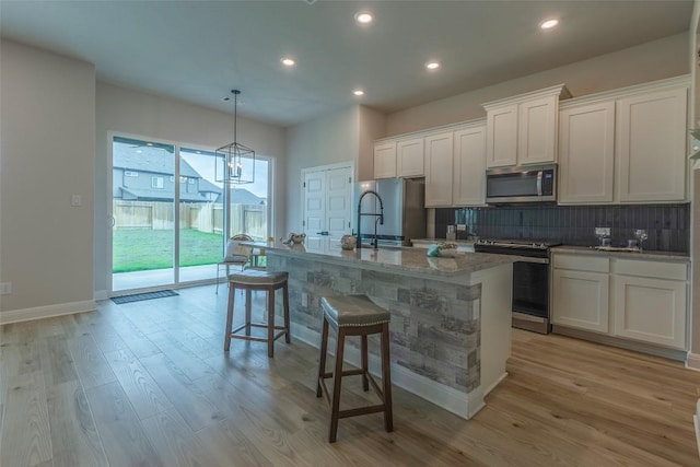 103 Periwinkle Ln, Bastrop, TX 78602 - kitchen featuring appliances with stainless steel finishes, backsplash, white cabinets, light wood finished floors, and an island with sink
