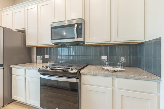 103 Periwinkle Ln, Bastrop, TX 78602 - kitchen featuring appliances with stainless steel finishes, backsplash, white cabinetry, light stone countertops, and light wood-type flooring