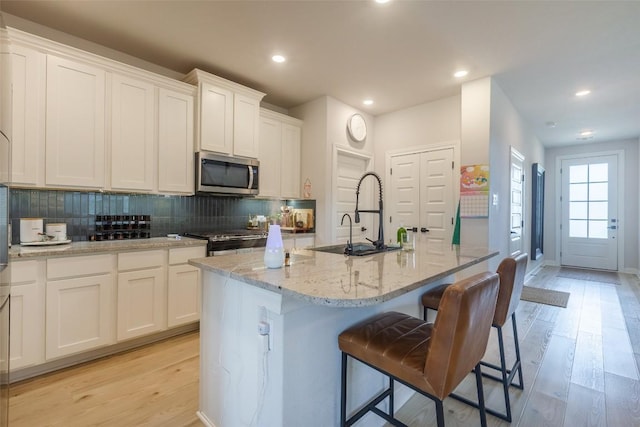 126 Periwinkle Ln, Bastrop, TX 78602 - kitchen featuring stainless steel appliances, light wood-style floors, white cabinetry, a center island with sink, and backsplash
