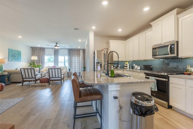 126 Periwinkle Ln, Bastrop, TX 78602 - kitchen featuring stainless steel appliances, open floor plan, light stone countertops, decorative backsplash, and white cabinetry
