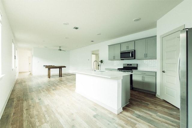 324 Millbrook Blvd, San Marcos, TX 78666 - kitchen with stainless steel appliances, light wood-type flooring, a ceiling fan, a center island with sink, and light countertops