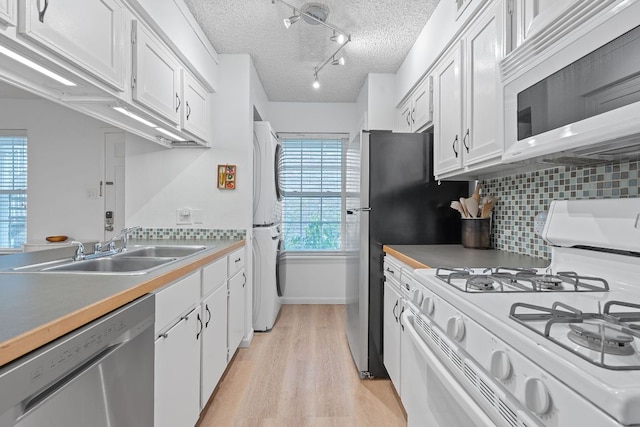 1240 Barton Hills Dr Unit 114, Austin, TX 78704 - kitchen featuring white appliances, stacked washer and clothes dryer, light wood-style floors, white cabinetry, and a textured ceiling