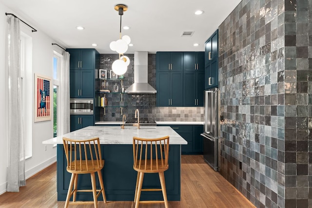606 Augusta Ave Unit 1, Austin, TX 78703 - kitchen with wall chimney exhaust hood, stainless steel appliances, light wood-type flooring, tasteful backsplash, and a kitchen breakfast bar