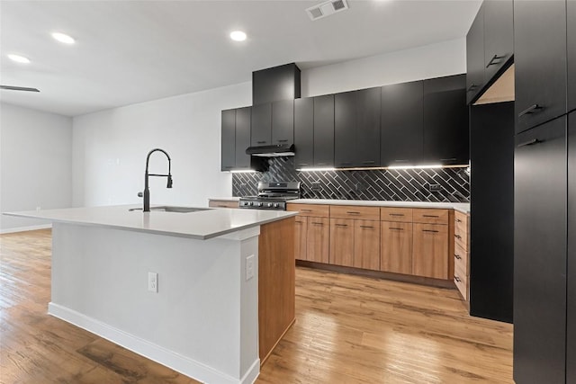 4510 Terry-O Ln Unit 415, Austin, TX 78745 - kitchen with stainless steel range, under cabinet range hood, decorative backsplash, a kitchen island with sink, and light wood-style floors