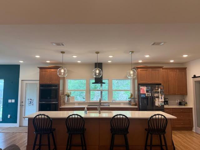 305 Goertz Dr, Red Rock, TX 78662 - kitchen with black appliances, wall chimney exhaust hood, light countertops, brown cabinets, and recessed lighting