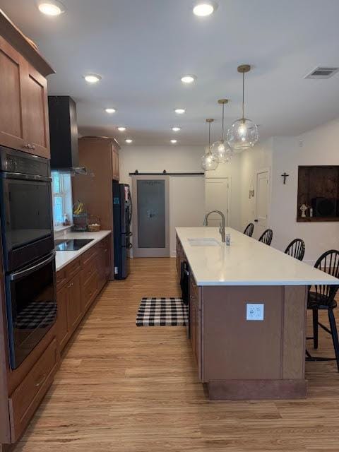 305 Goertz Dr, Red Rock, TX 78662 - kitchen featuring black appliances, a barn door, a breakfast bar area, light wood-style flooring, and a kitchen island with sink