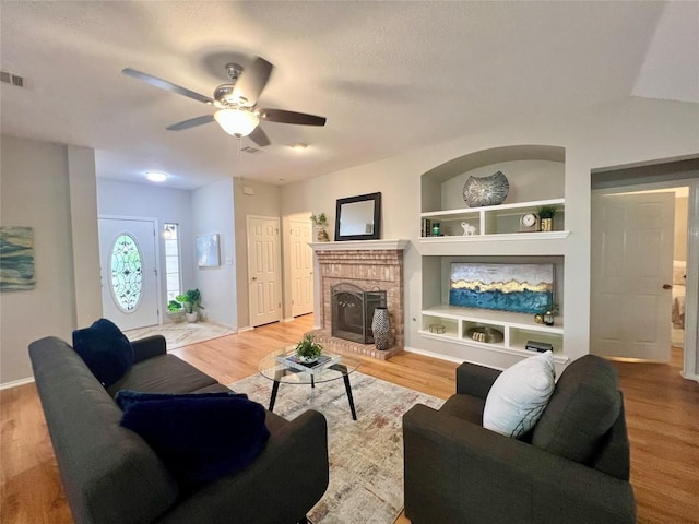 612 Thrush Dr, Leander, TX 78641 - living area with built in shelves, a ceiling fan, a fireplace, light wood-style floors, and a textured ceiling