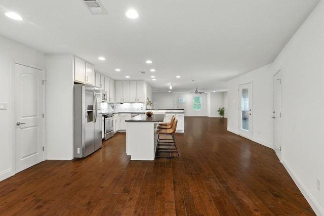 1612 Westmoor Dr, Austin, TX 78723 - kitchen featuring appliances with stainless steel finishes, dark wood-style flooring, a breakfast bar area, recessed lighting, and white cabinetry