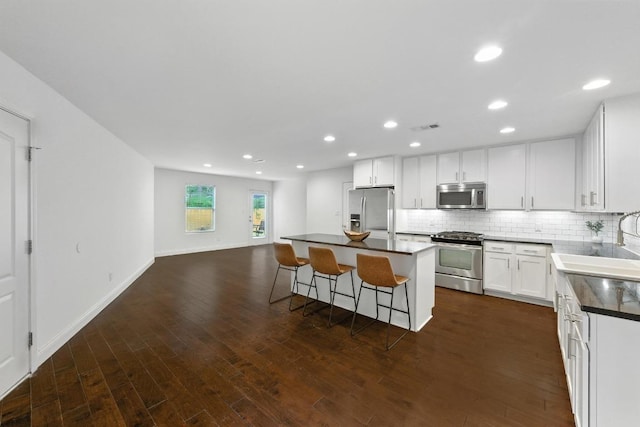 1612 Westmoor Dr, Austin, TX 78723 - kitchen featuring appliances with stainless steel finishes, dark countertops, a kitchen breakfast bar, backsplash, and dark wood-style floors