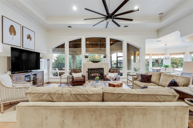 1307 Osprey Ridge Loop, Lago Vista, TX 78645 - living area featuring a fireplace, a raised ceiling, a ceiling fan, light wood-style floors, and crown molding