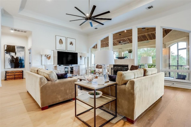 1307 Osprey Ridge Loop, Lago Vista, TX 78645 - living room featuring light wood finished floors, a ceiling fan, a raised ceiling, a fireplace, and crown molding