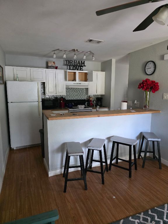 2124 Burton Dr Unit 208, Austin, TX 78741 - kitchen with freestanding refrigerator, under cabinet range hood, black microwave, dark wood-style flooring, and white cabinetry