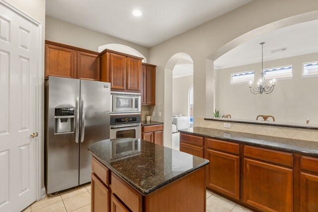 15325 Interlachen Dr, Austin, TX 78717 - kitchen with stainless steel appliances, arched walkways, light tile patterned floors, dark stone counters, and brown cabinetry