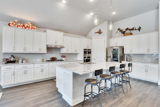 2817 Mossy Springs Dr, Leander, TX 78641 - kitchen with stainless steel appliances, under cabinet range hood, decorative backsplash, white cabinetry, and a breakfast bar