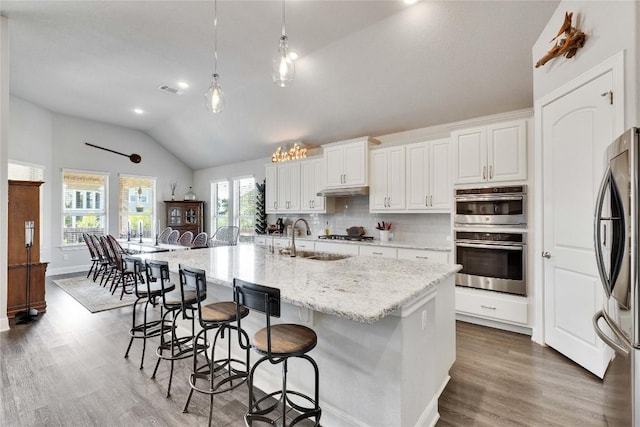 2817 Mossy Springs Dr, Leander, TX 78641 - kitchen with lofted ceiling, appliances with stainless steel finishes, wood finished floors, a kitchen bar, and white cabinets