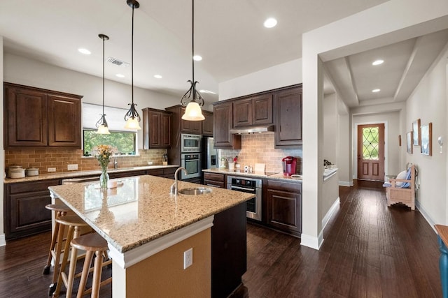 29 Prestonwood Cir, Lakeway, TX 78734 - kitchen with stainless steel appliances, under cabinet range hood, a kitchen island with sink, dark brown cabinetry, and dark wood-style flooring