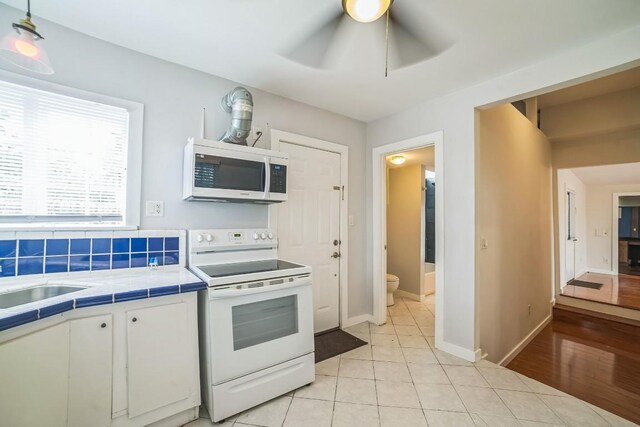 15102 Iowa St, Austin, TX 78734 - kitchen featuring white appliances, tile countertops, white cabinetry, ceiling fan, and light tile patterned flooring
