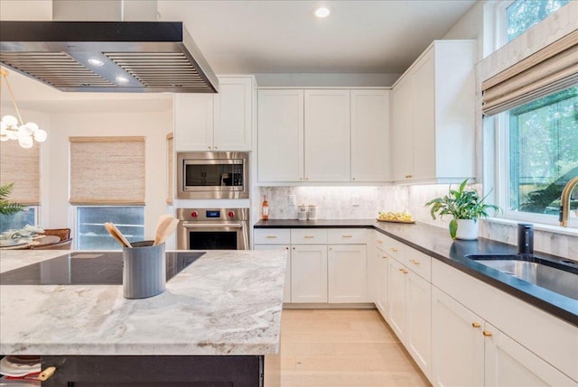 9110 Scotsman Dr, Austin, TX 78750 - kitchen with stainless steel appliances, wall chimney range hood, white cabinetry, backsplash, and light wood-style flooring