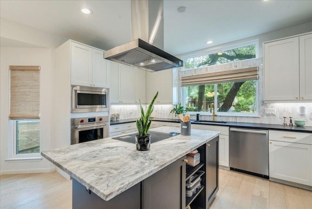 9110 Scotsman Dr, Austin, TX 78750 - kitchen featuring stainless steel appliances, island exhaust hood, light wood finished floors, decorative backsplash, and dark stone counters
