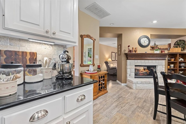 35 Forest Mesa, Round Rock, TX 78664 - kitchen featuring white cabinets, dark countertops, tasteful backsplash, a stone fireplace, and light wood-style floors