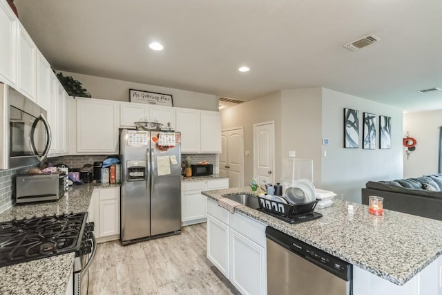 18430 Stevie Ray Dr, Round Rock, TX 78664 - kitchen featuring appliances with stainless steel finishes, white cabinets, light wood-type flooring, light stone countertops, and backsplash