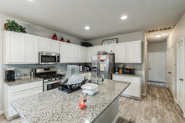 18430 Stevie Ray Dr, Round Rock, TX 78664 - kitchen with appliances with stainless steel finishes, white cabinets, light wood-style flooring, an island with sink, and tasteful backsplash