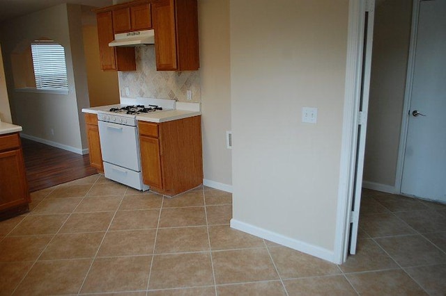 205 E Mitchell Dr, Hutto, TX 78634 - kitchen with white gas range oven, under cabinet range hood, brown cabinetry, tasteful backsplash, and light countertops